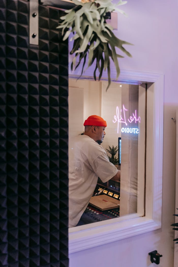 services-03 Man working on a sound mixer in a recording studio, wearing a red beanie.